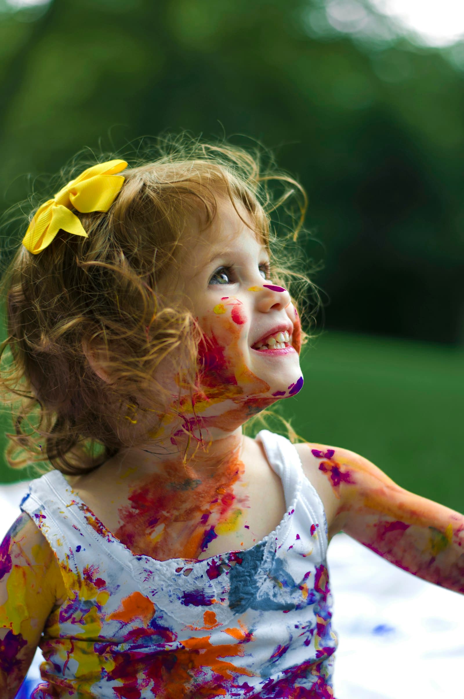 A little girl covered in paint, laughing outdoors