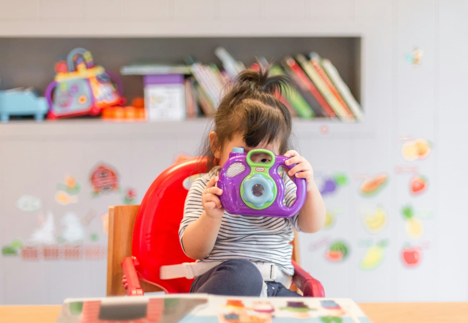 A toddler in a playroom holding a toy camera
