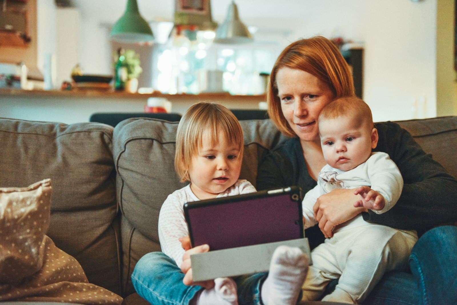 A caregiver on the sofa at home with a toddler and a baby on her lap